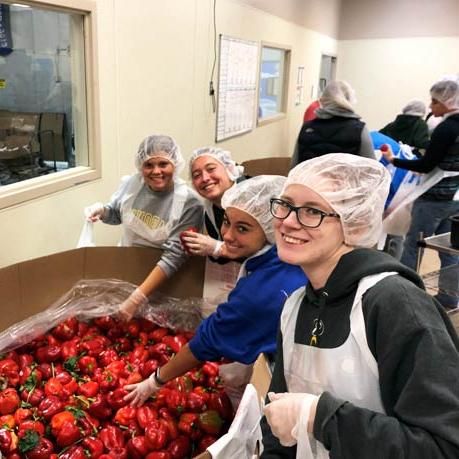 Volunteers smiling next to giant crate of red peppers